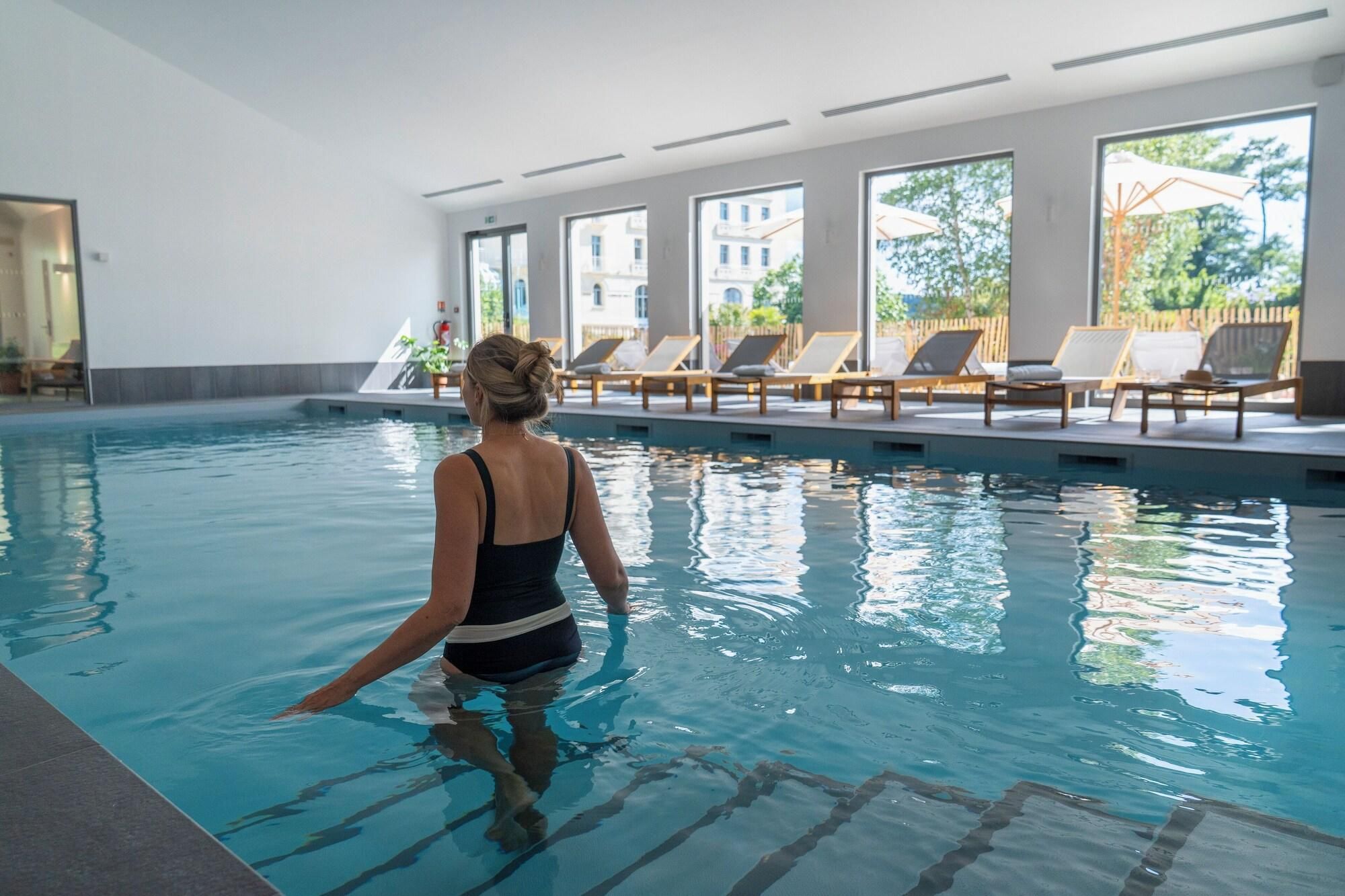 Una piscina interior amb aigua cristal·lina, una persona a la piscina i gandules al fons.