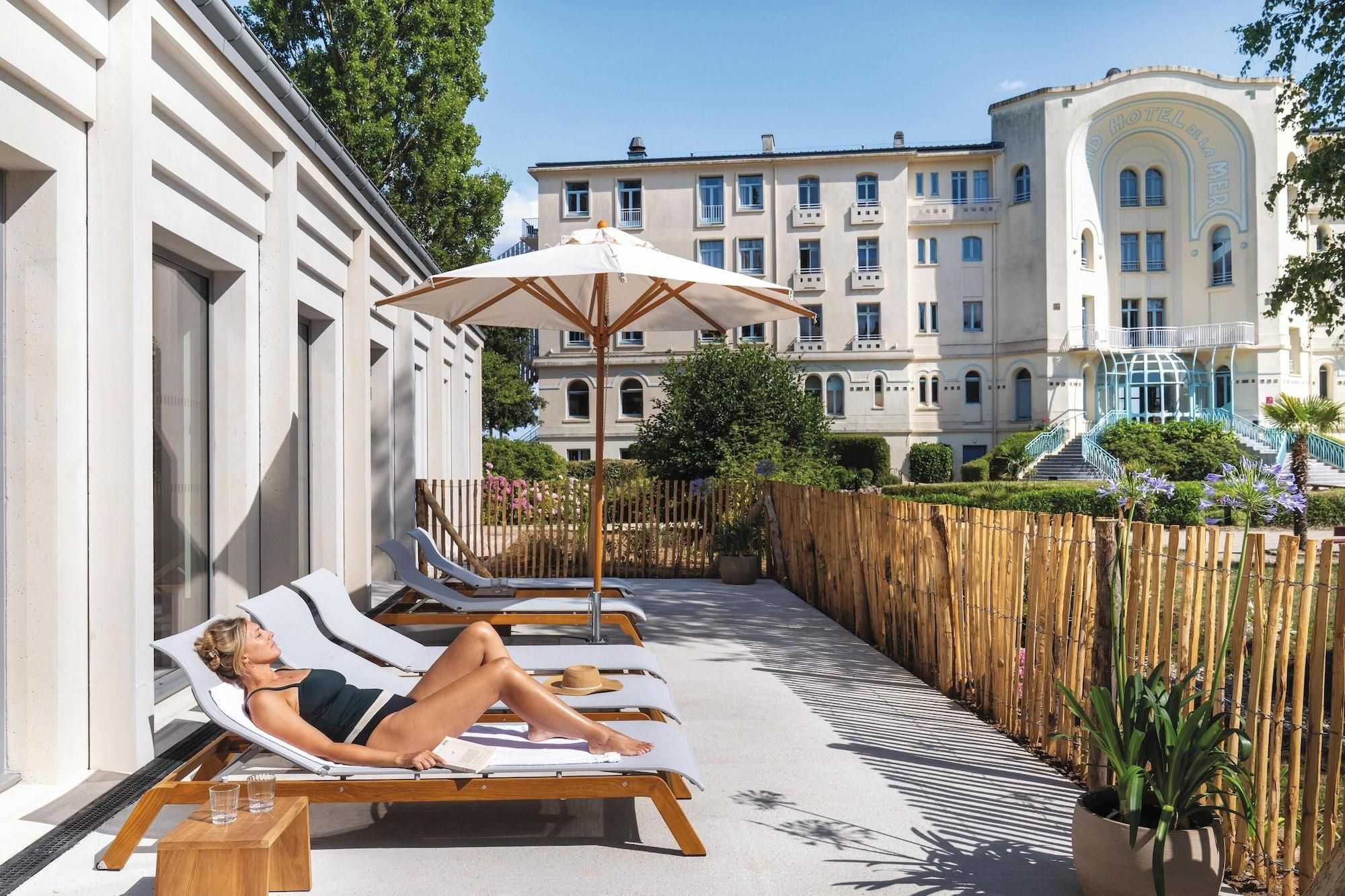 A hotel with a pool area featuring sun loungers and a wooden deck.