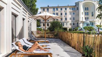 A hotel with a pool area featuring sun loungers and a wooden deck.