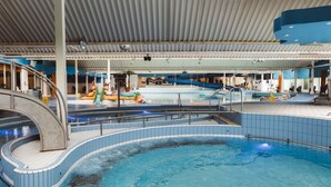 Une piscine intérieure avec un toboggan, des espaces de détente et un toit abrité.