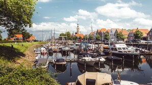 Un port de plaisance avec des bateaux amarrés, une jetée en bois et, au fond, des bâtiments aux toits rouges.
