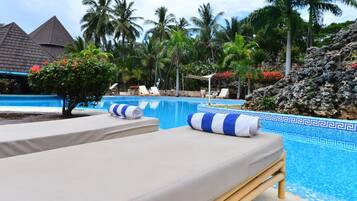 Un área junto a la piscina con sillones de descanso, un árbol pequeño y un paisaje rocoso.