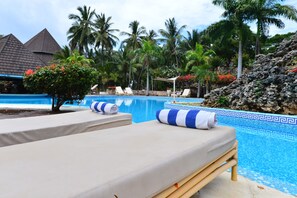 A poolside area with lounge chairs, a small tree, and a rocky landscape. - Diani Reef Beach Resort & Spa (Diani Beach)