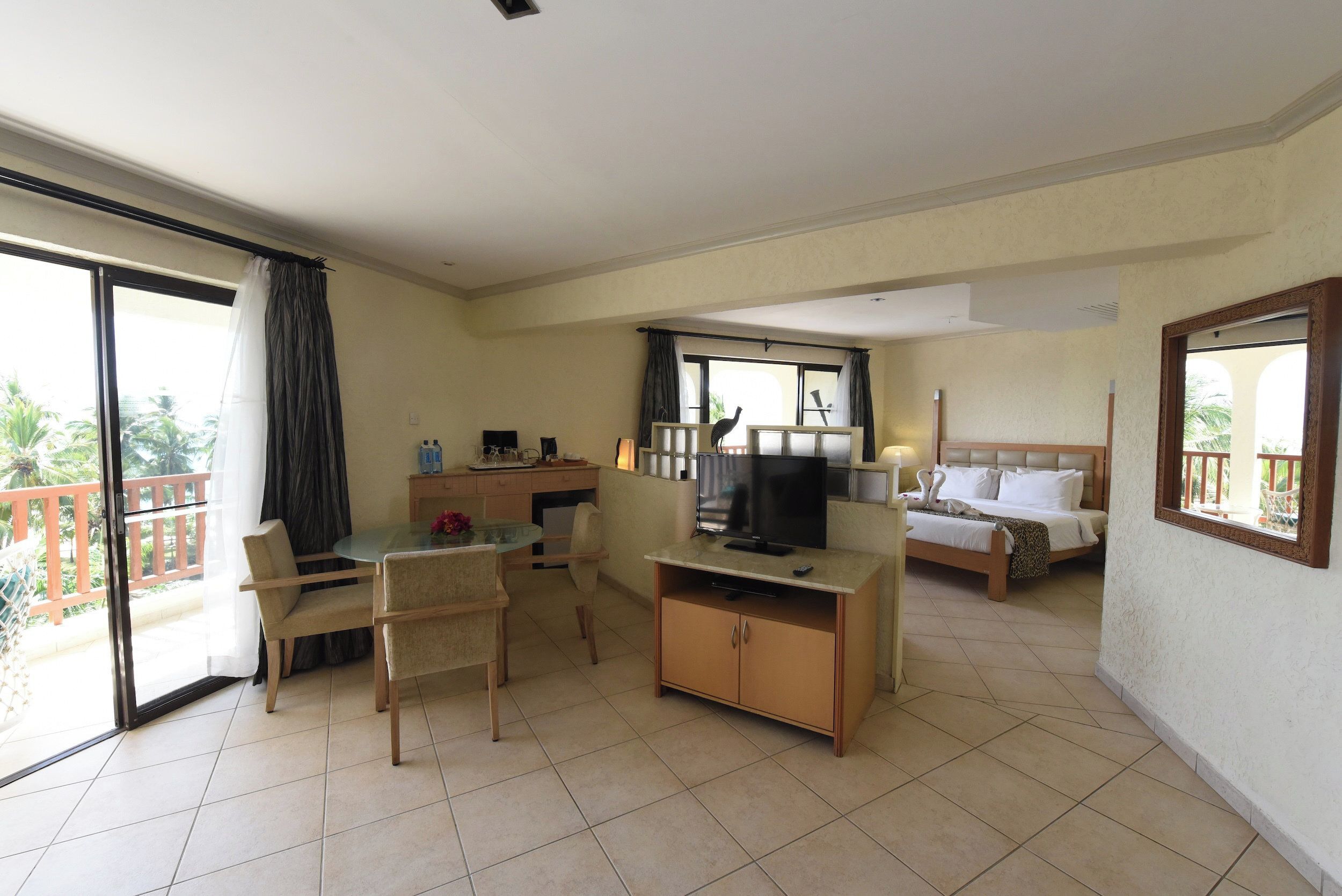 A hotel room with a balcony, a dining area, a TV, and a bed.