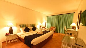 A hotel room with a bed, two bedside tables with lamps, a chair, a small table, and a mirror on the wall. - Diani Reef Beach Resort & Spa (Diani Beach)