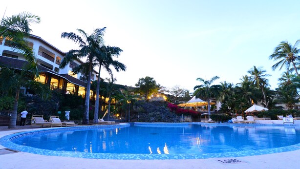 A swimming pool with lounge chairs, palm trees, and a building with balconies. - Diani Reef Beach Resort & Spa (Diani Beach)