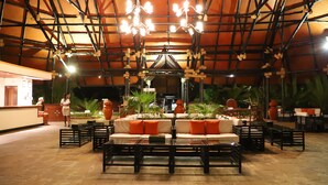 An indoor seating area with tables, chairs, and a central sofa with orange cushions. - Diani Reef Beach Resort & Spa (Diani Beach)