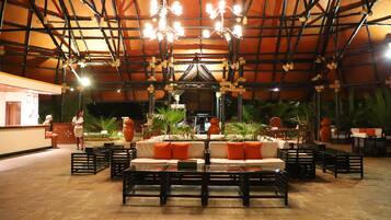 An indoor seating area with tables, chairs, and a central sofa with orange cushions.