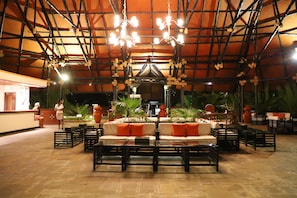 An indoor seating area with tables, chairs, and a central sofa with orange cushions.