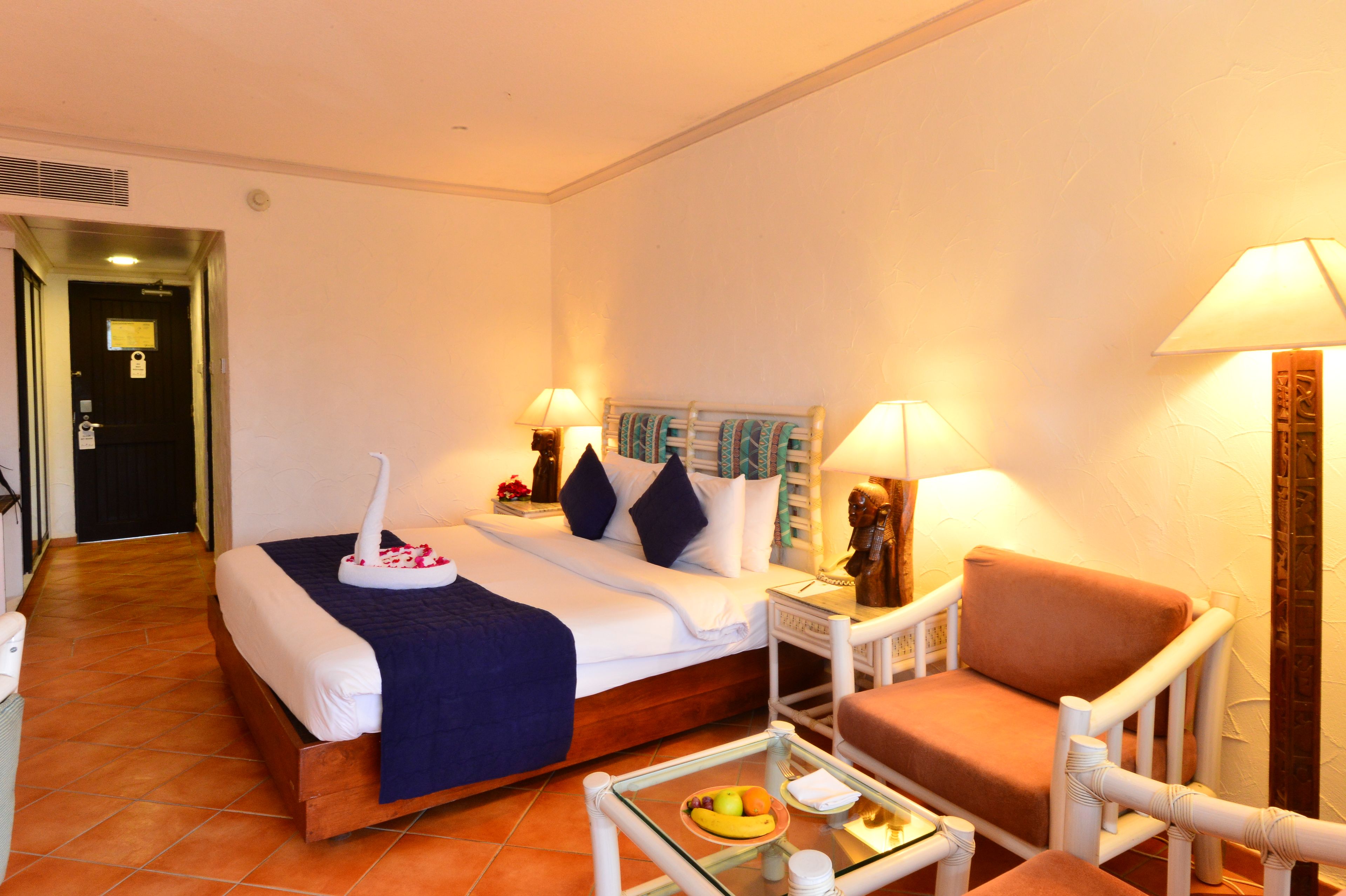 A hotel room with a bed, a chair, a small table with fruit, and two lamps.