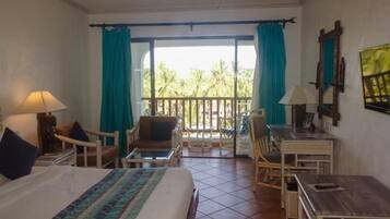 A hotel room with a bed, a desk, a chair, and a balcony with curtains.