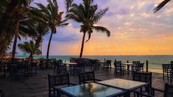 An outdoor seating area with tables and chairs, palm trees, and a view of the ocean.
