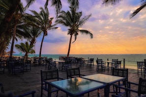 An outdoor seating area with tables and chairs, palm trees, and a view of the ocean.
