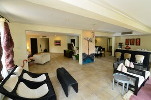 A spacious living area with a sofa, a bench, and a dining area with chairs and a table. - Diani Reef Beach Resort & Spa (Diani Beach)