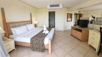 A hotel room with a bed, bedside table, lamp, TV, desk, and wardrobe.