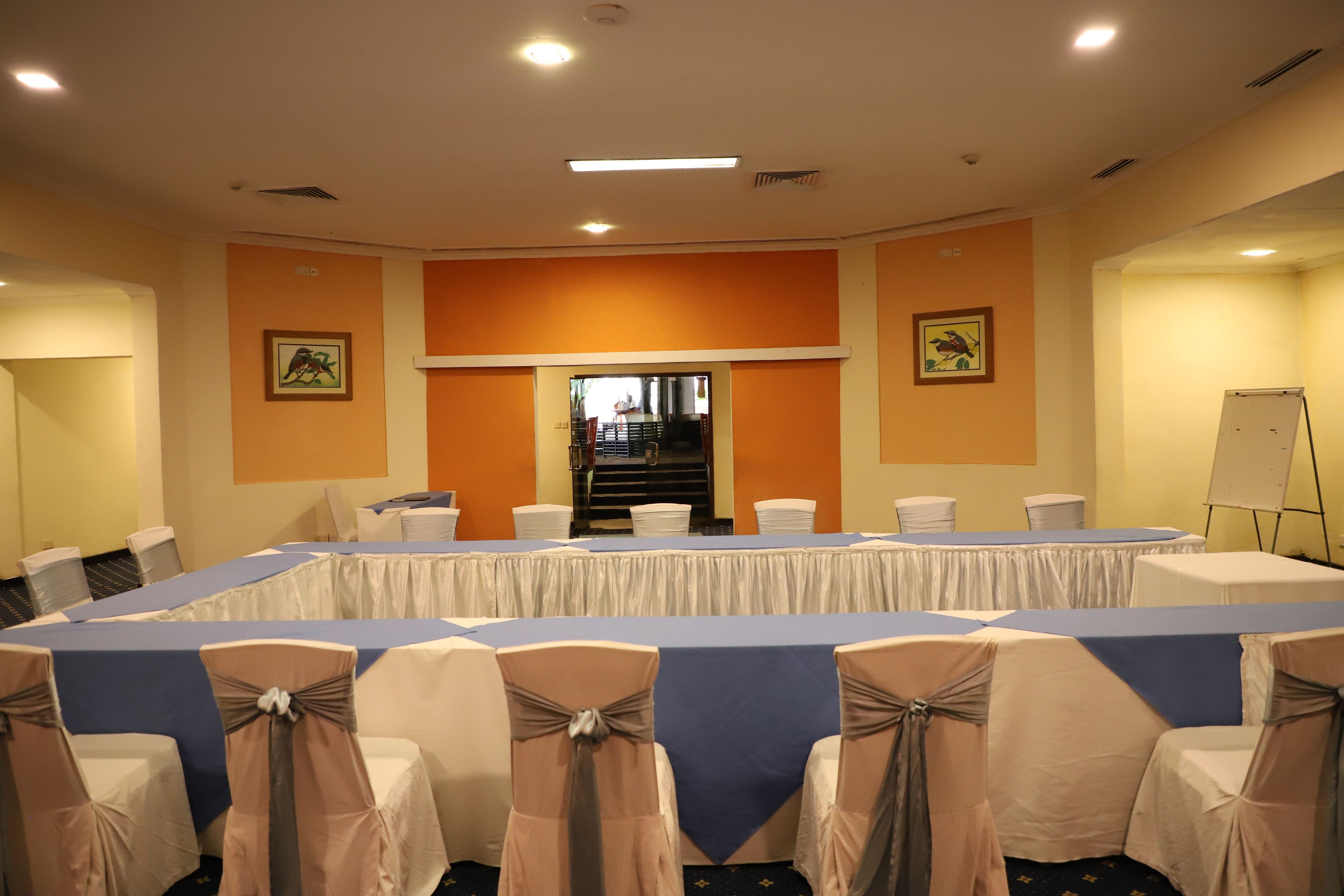 Un salón de conferencias con una larga mesa, sillas adornadas con cintas y una pizarra.