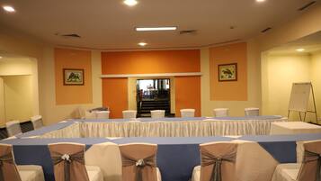 Un salón de conferencias con una larga mesa, sillas adornadas con cintas y una pizarra.