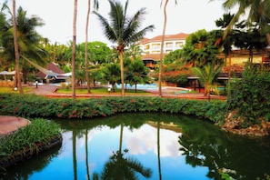 A resort with a swimming pool, palm trees, and a building with a red roof.