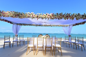 A beach wedding setup with white chairs and a floral canopy. - Diani Reef Beach Resort & Spa (Diani Beach)
