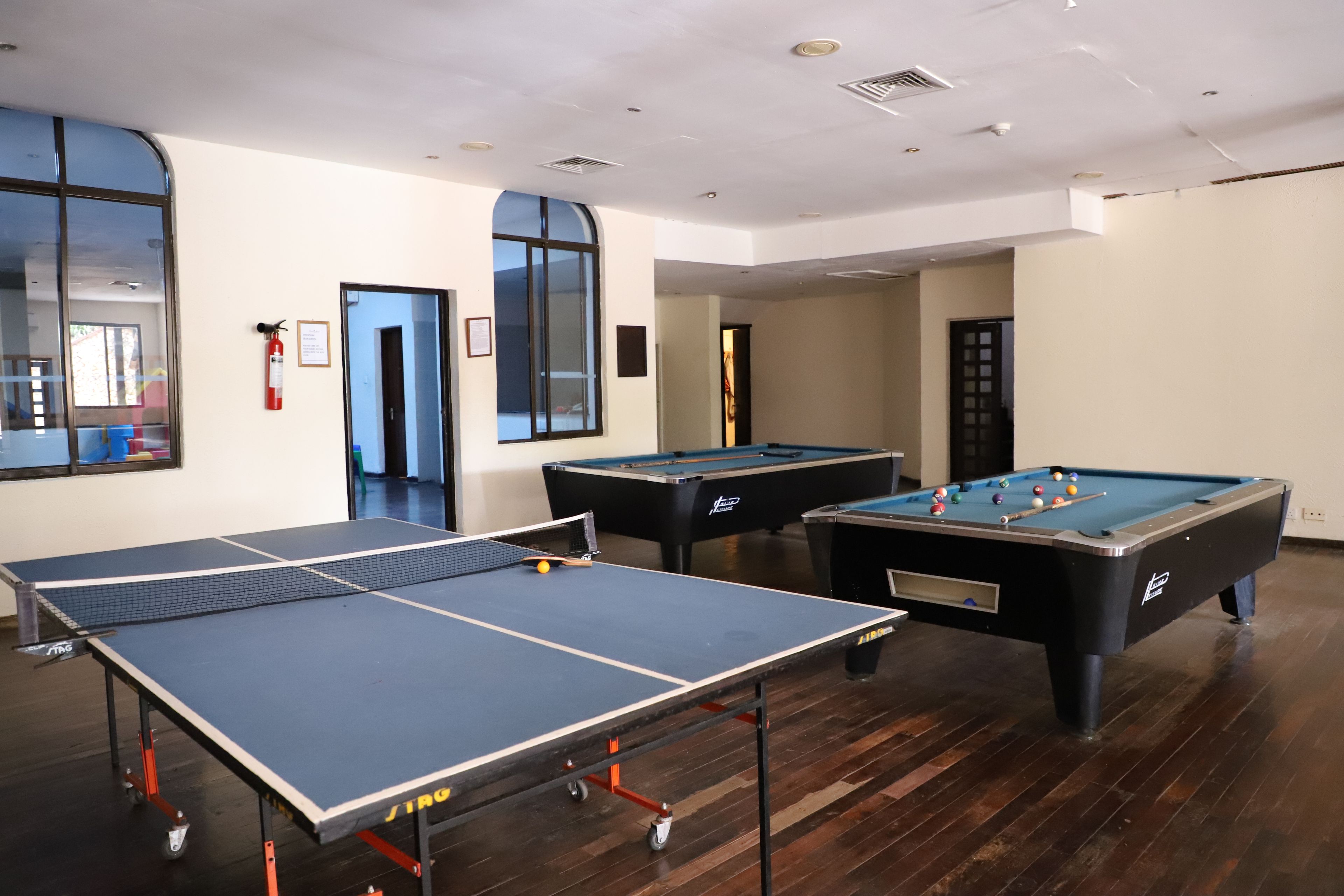 A room with a ping pong table, two pool tables, and a fire extinguisher.