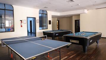 A room with a ping pong table, two pool tables, and a fire extinguisher.
