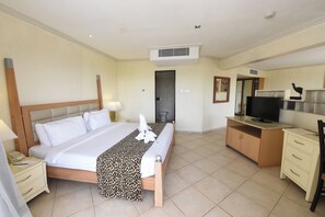 A hotel room with a bed, bedside table, lamp, television, and a desk with a chair. - Diani Reef Beach Resort & Spa (Diani Beach)