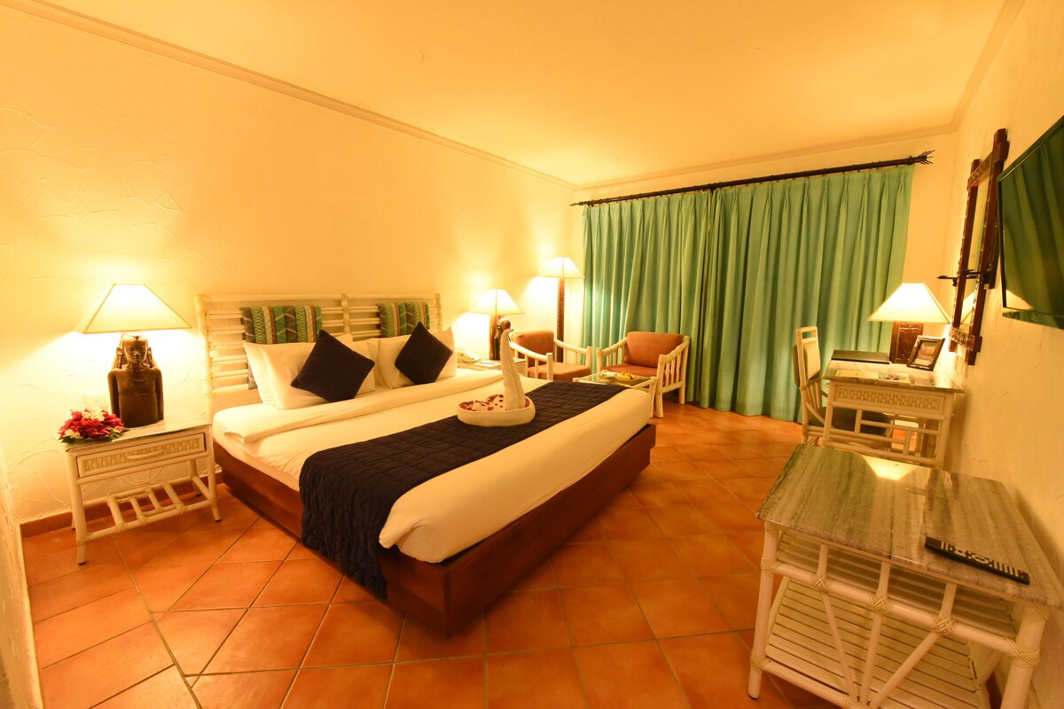 A hotel room with a large bed, two bedside tables with lamps, a chair, a small table with a lamp, and a mirror on the wall.