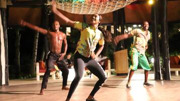 A group of people performing a dance in an outdoor setting with a wooden floor and a covered area.