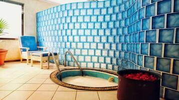 A small indoor pool with a tiled wall, a chair, and a potted plant.