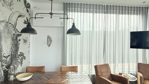 Un comedor con una gran mesa de madera, sillas tapizadas en tonos marrones, una lámpara colgante moderna y un televisor de pantalla plana grande.