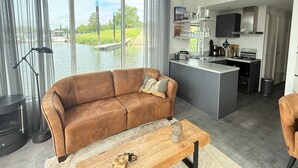 Una sala de estar moderna con un sofá, una mesa de centro y vistas a una masa de agua a través de ventanas amplias.