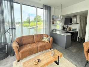 Ein modernes Wohnzimmer mit einer Couch, einem Couchtisch und Blick auf ein Gewässer durch große Fenster.