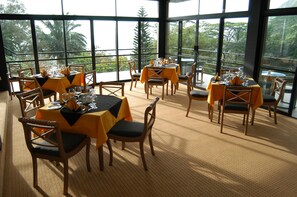 A restaurant with multiple tables and chairs, large windows, and a view of greenery. - Hunas Falls (Kandy)