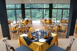 A restaurant with tables set for dining, large windows offering a view of greenery, and a modern interior design. - Hunas Falls (Kandy)