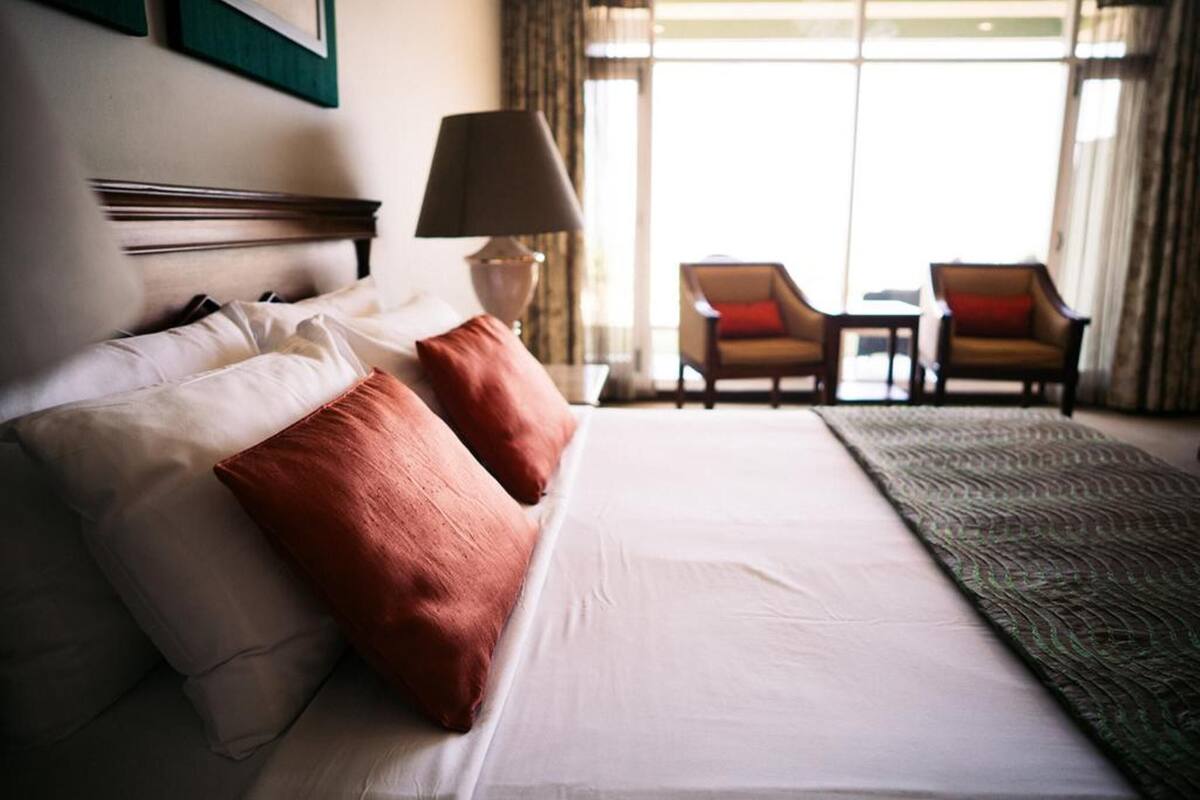 Quarto de hotel com cama, duas cadeiras, uma mesa e um abajur.