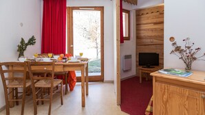 Ein Zimmer mit Esstisch, Stühlen, einem Fernseher und einem Fenster mit rotem Vorhang.