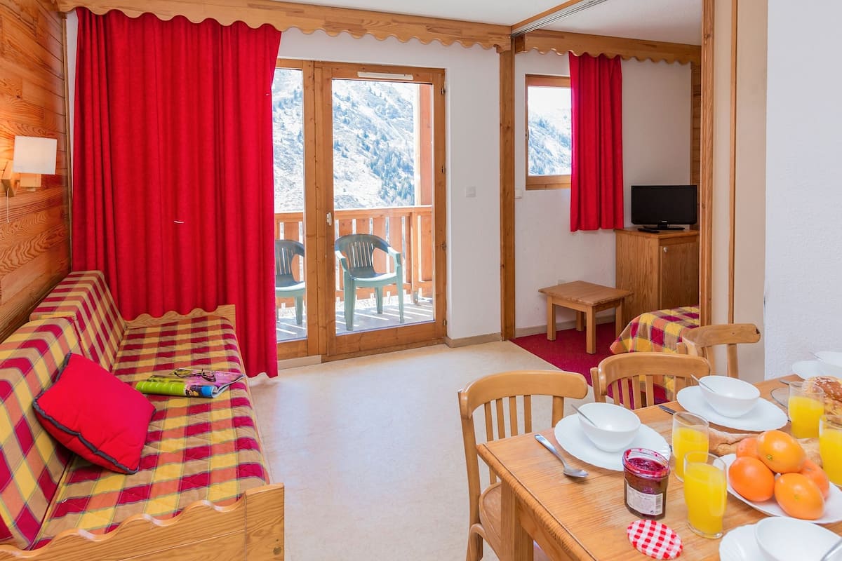 A cozy room with a sofa, dining table, chairs, and a TV.