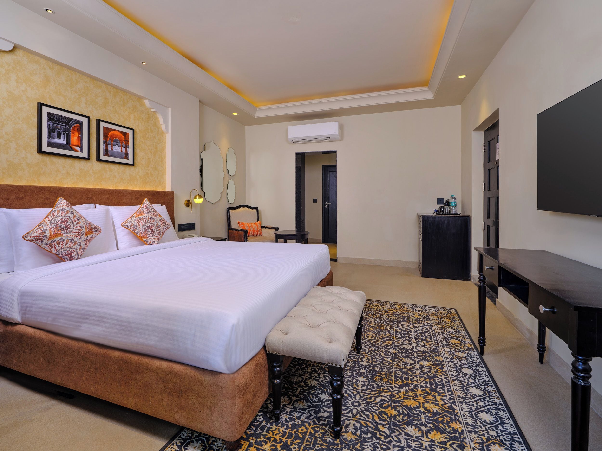 A hotel room with a large bed, a bench, a TV, and a patterned rug.