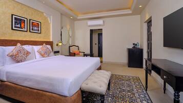 A hotel room with a large bed, a bench, a TV, and a patterned rug.