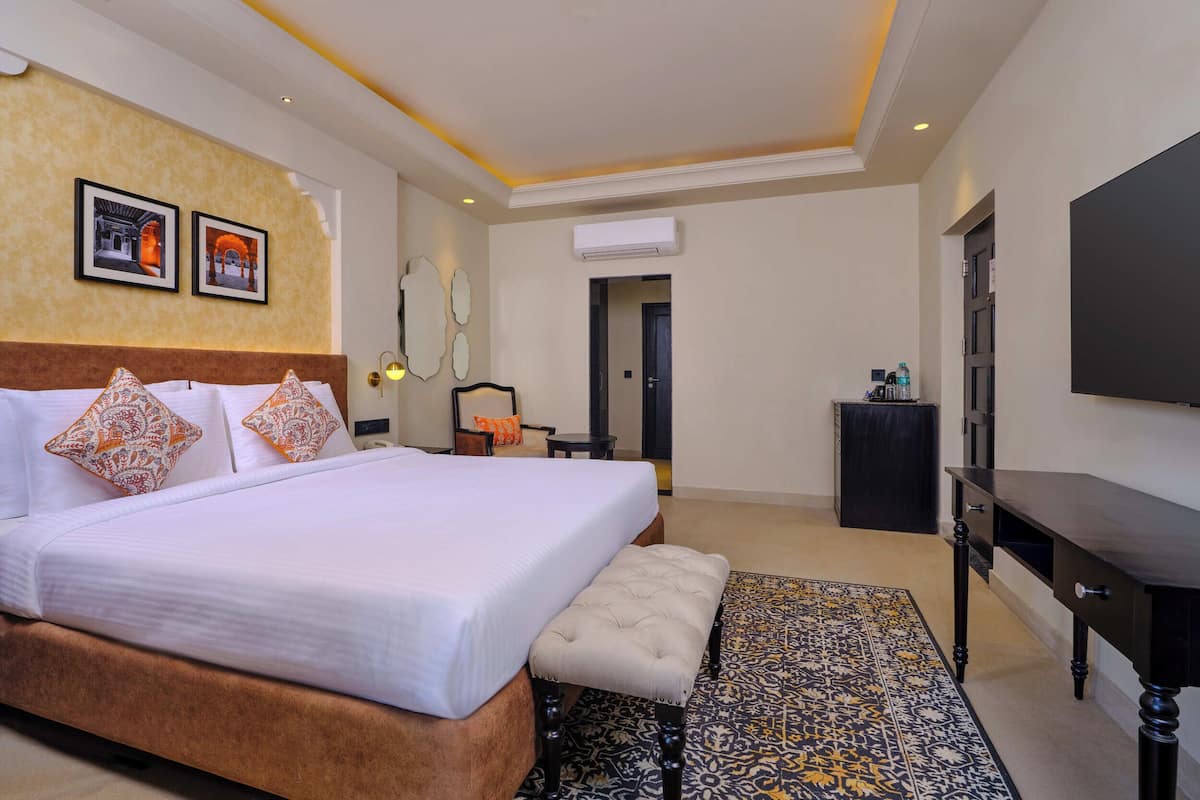A hotel room with a large bed, a bench, a TV, and a patterned rug.