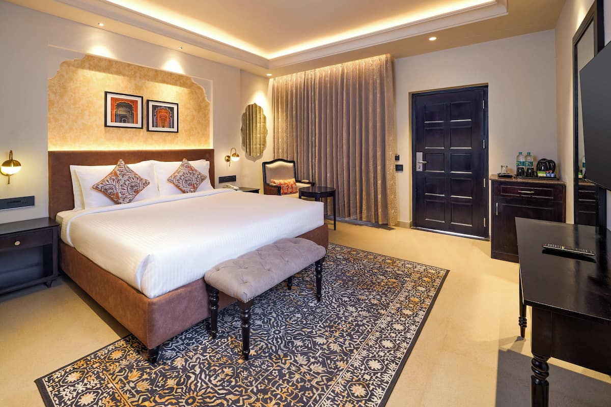 A well-lit hotel room with a large bed, a bench, a desk, and a wardrobe.