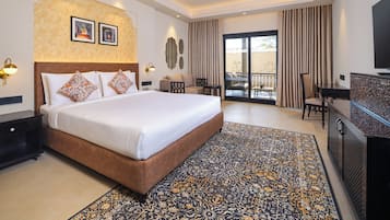 Habitación de hotel con una cama grande, un escritorio, televisión y balcón con cortinas.