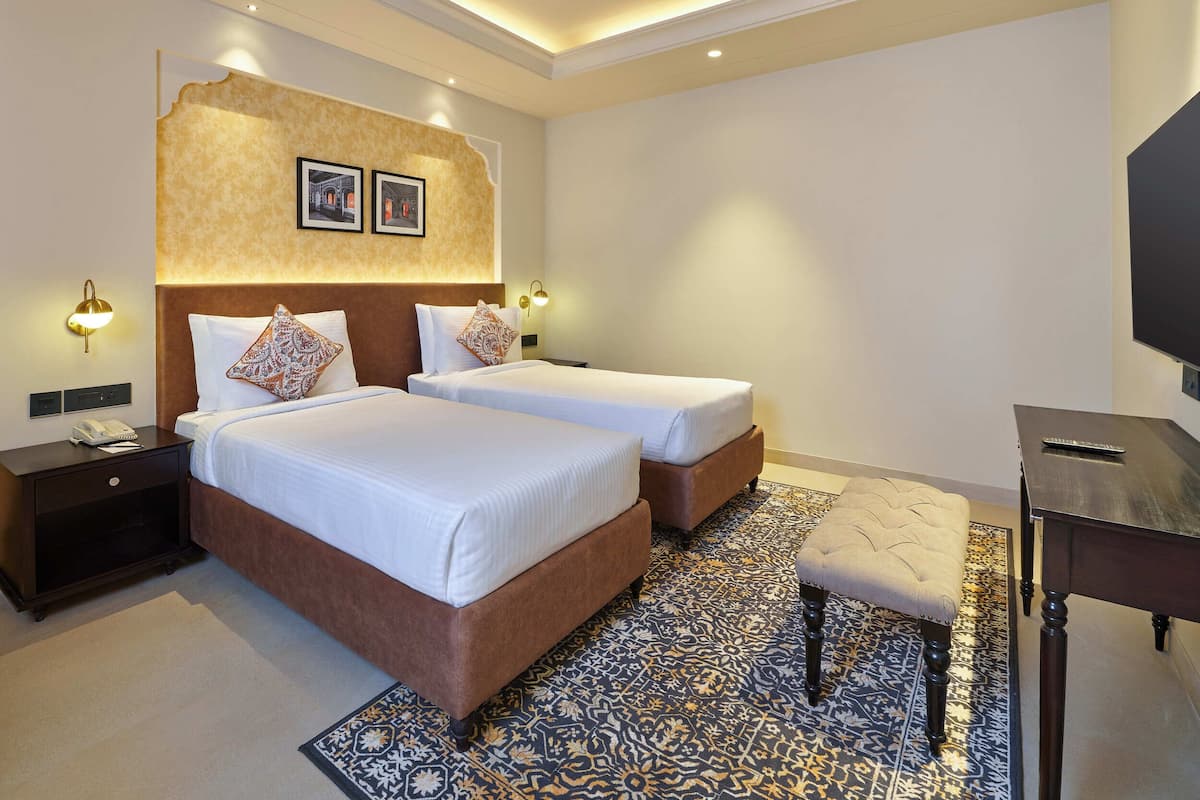 A hotel room with two beds, a desk, a television, and a patterned rug.