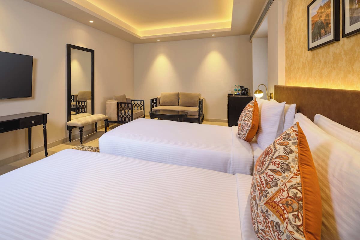 A hotel room with two beds, a desk, a chair, a sofa, a TV, and a mirror.