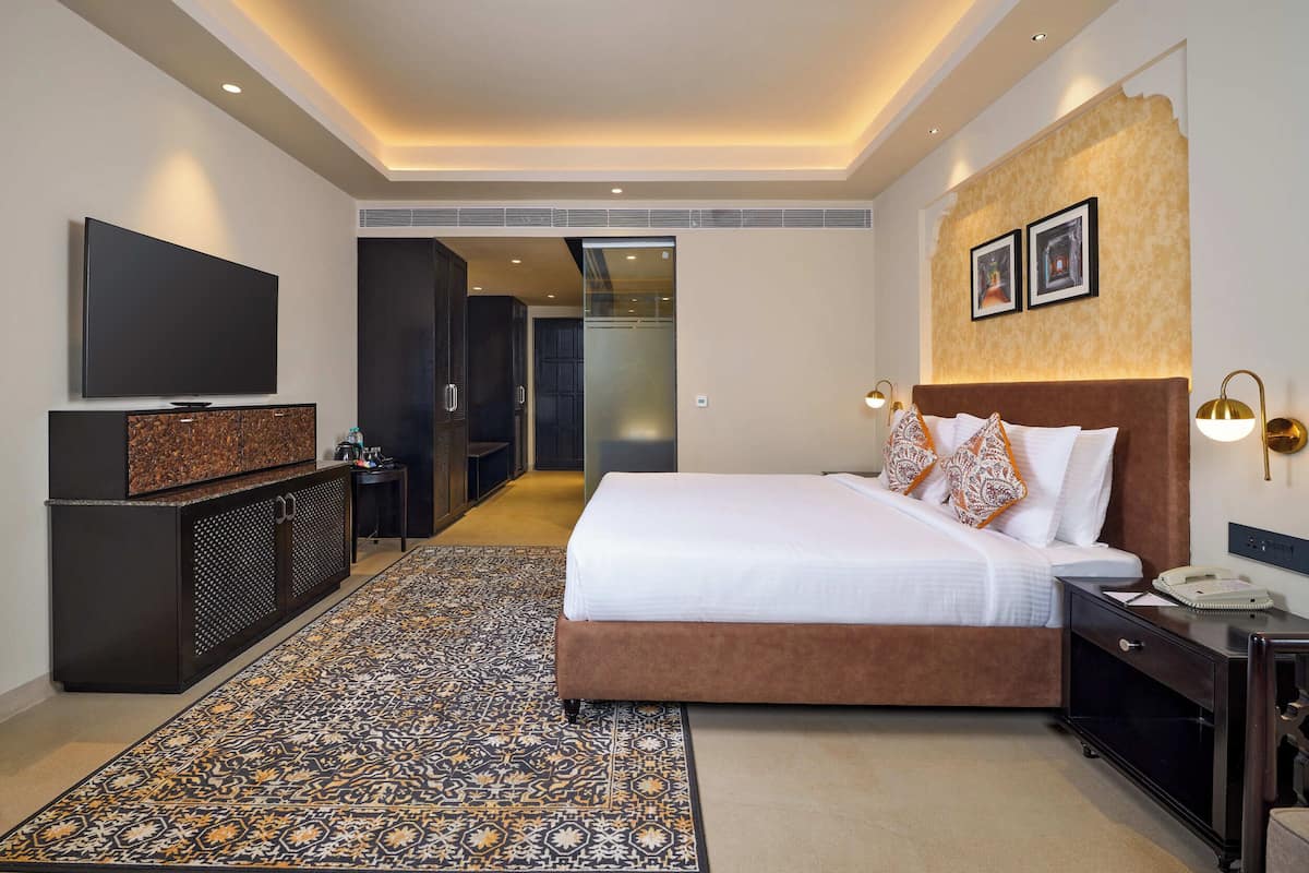 A modern hotel room with a large bed, a television, a desk, and a walk-in closet.