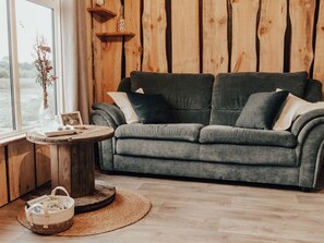 Ein gemütliches Zimmer mit einem grauen Sofa, einem runden Holztisch und Blick ins Freie.