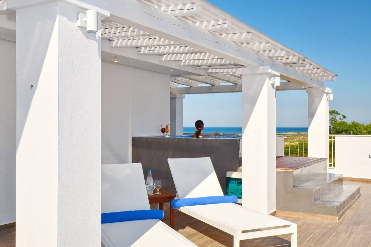 A covered outdoor seating area with white chairs and a pool view.