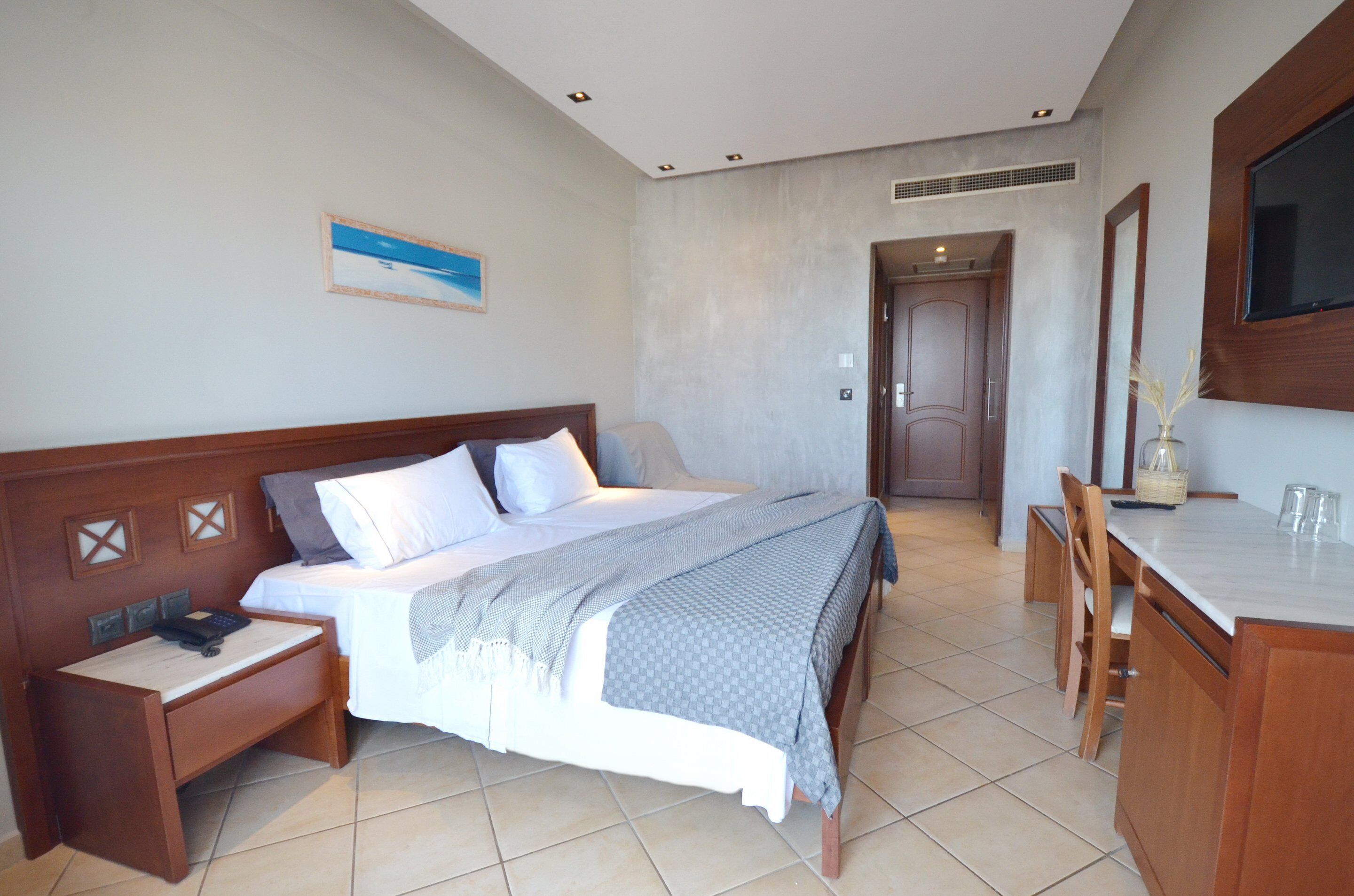 A hotel room with a bed, bedside table, desk, chair, and a TV mounted on the wall.