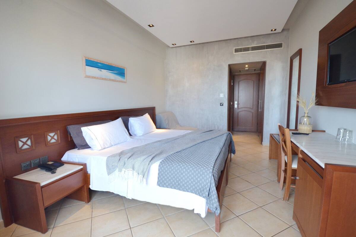 A hotel room with a bed, bedside table, desk, chair, and a TV mounted on the wall.