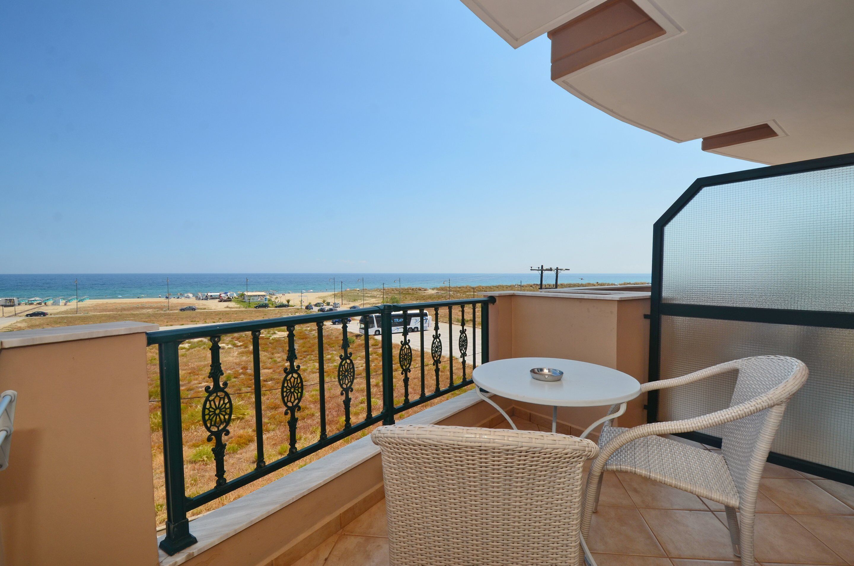 A balcony with a view of the beach, a table, and wicker chairs.